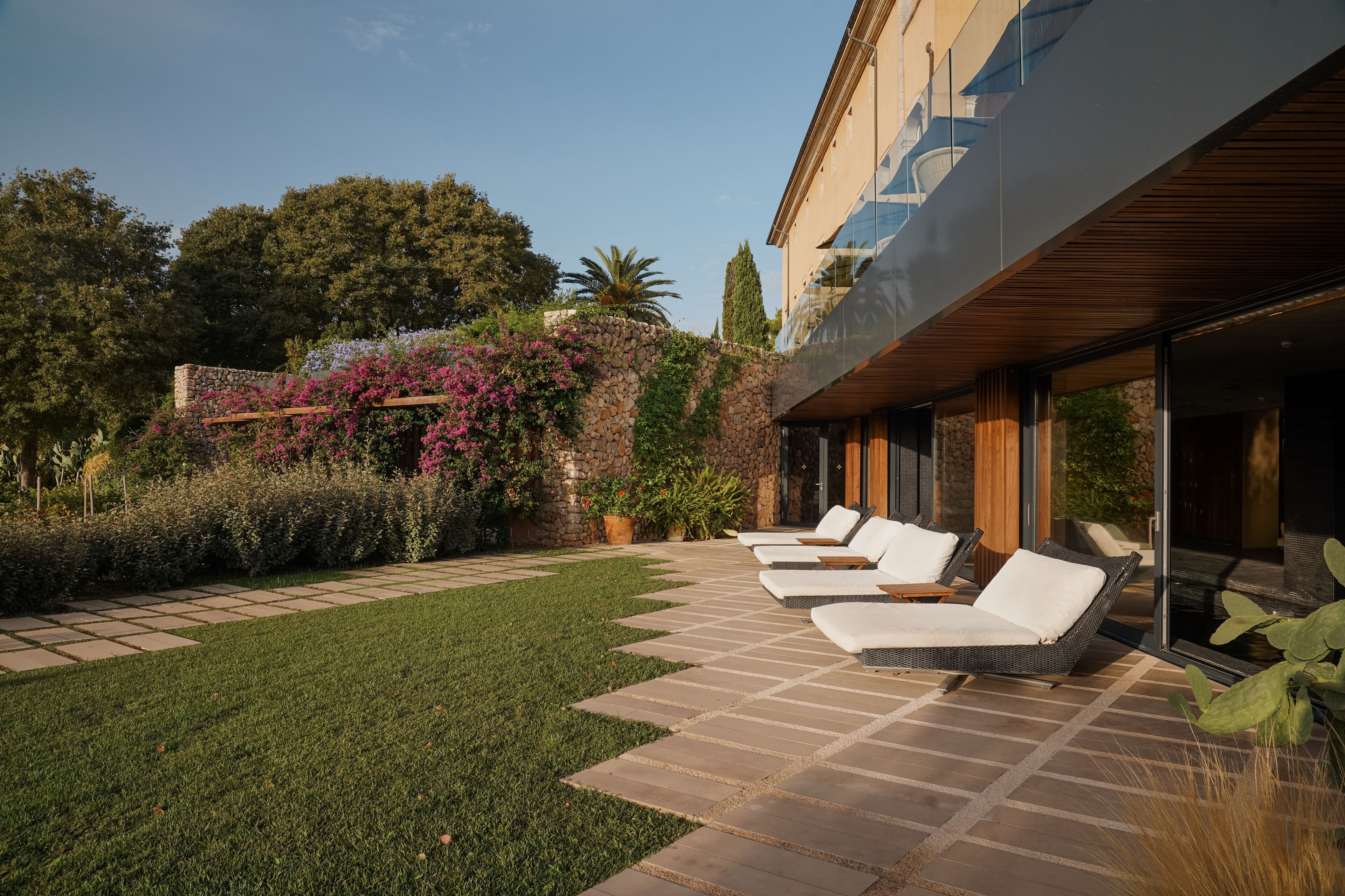 Un patio moderno al aire libre con un sendero de piedra que lleva a una zona de estar con sillones blancos.