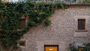 A stone building with a warm interior light, a number '3' sign, and potted plants around the entrance. - Son Brull Hotel & Spa (Pollenca)