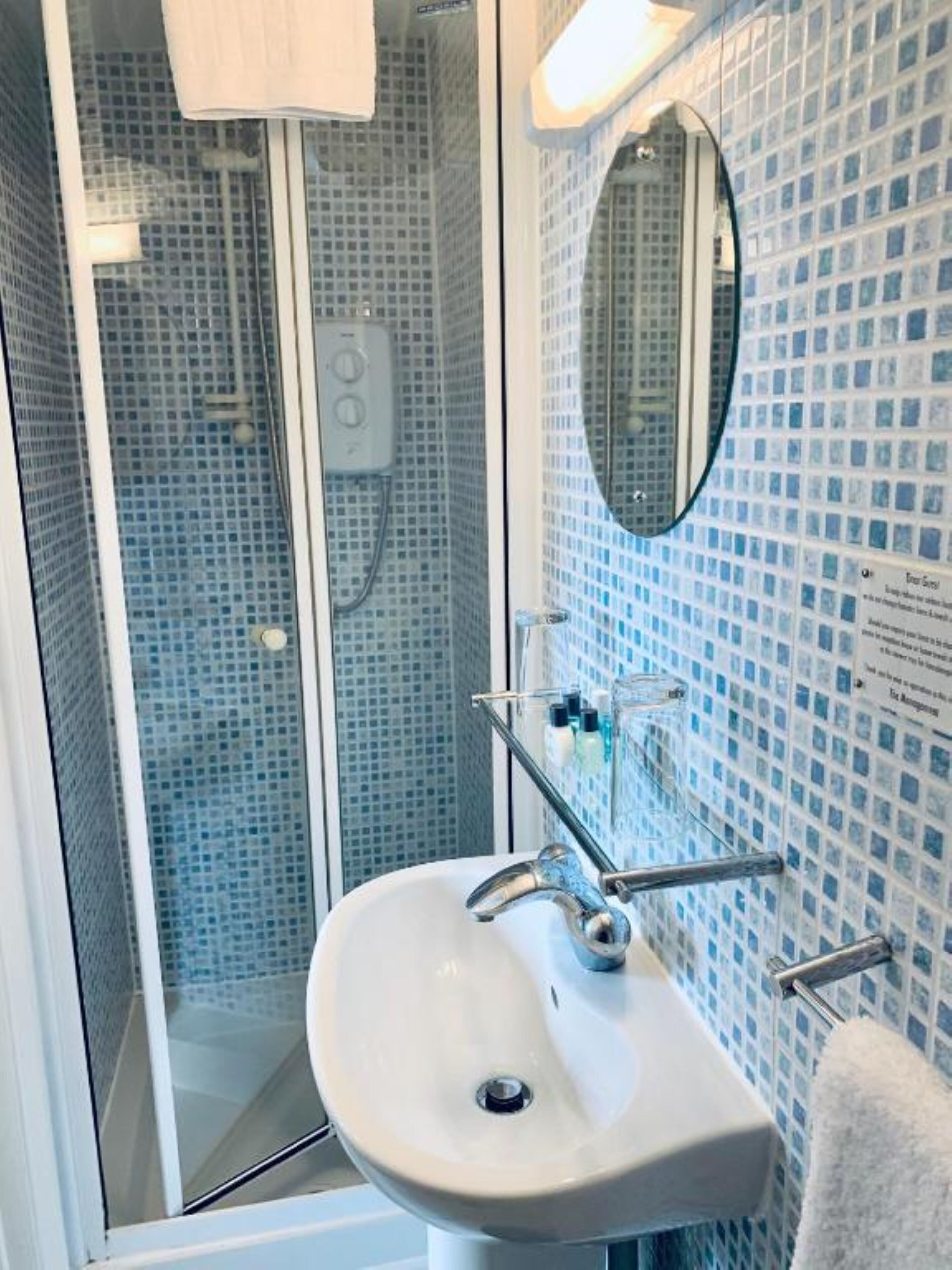 A bathroom with a glass-enclosed shower, a white sink with a chrome faucet, and a tiled wall with a mirror.
