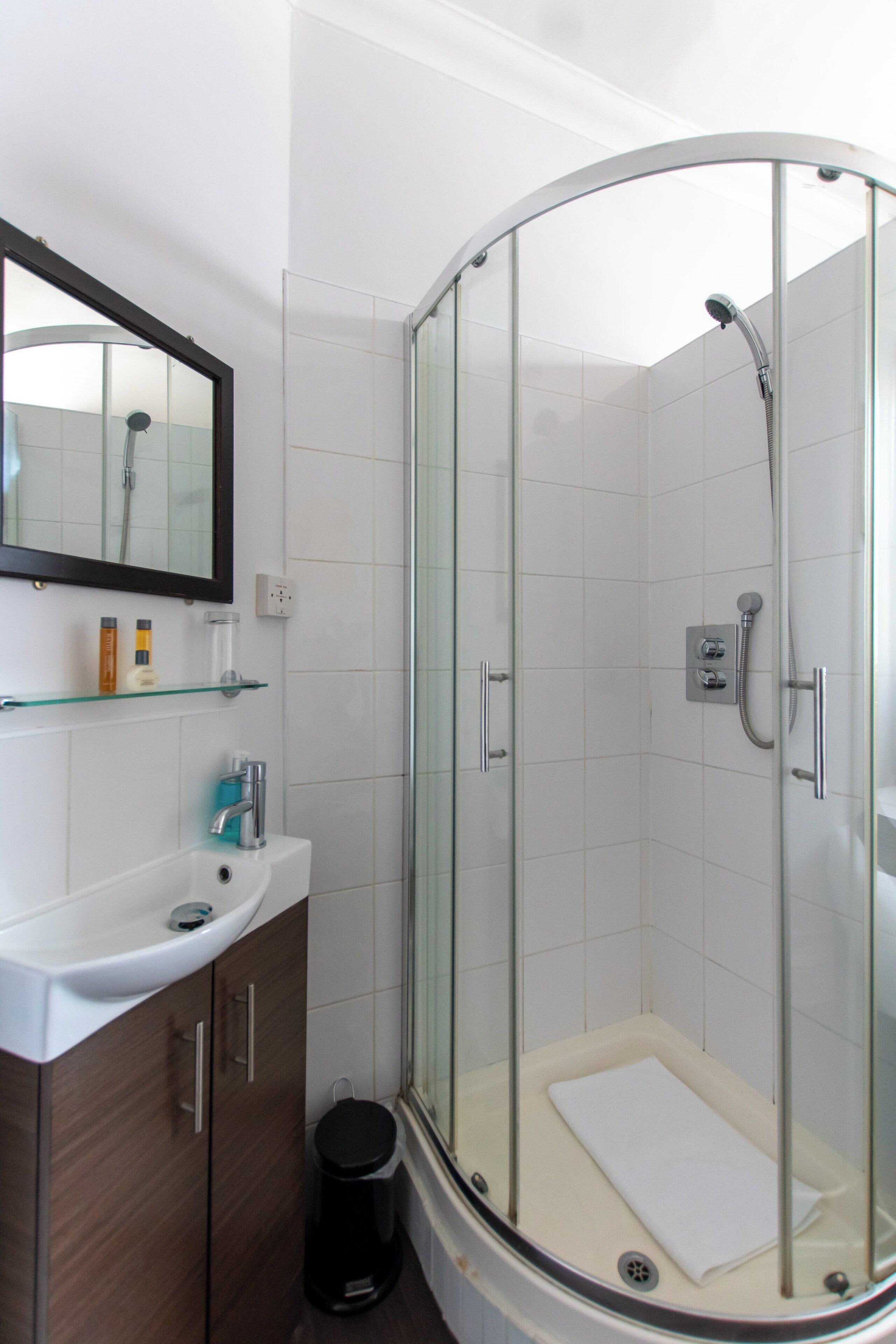 A modern bathroom with a glass-enclosed shower, a white sink, and a mirror above it.
