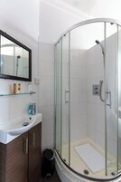Un baño moderno con ducha de vidrio, un lavabo blanco y un espejo encima.