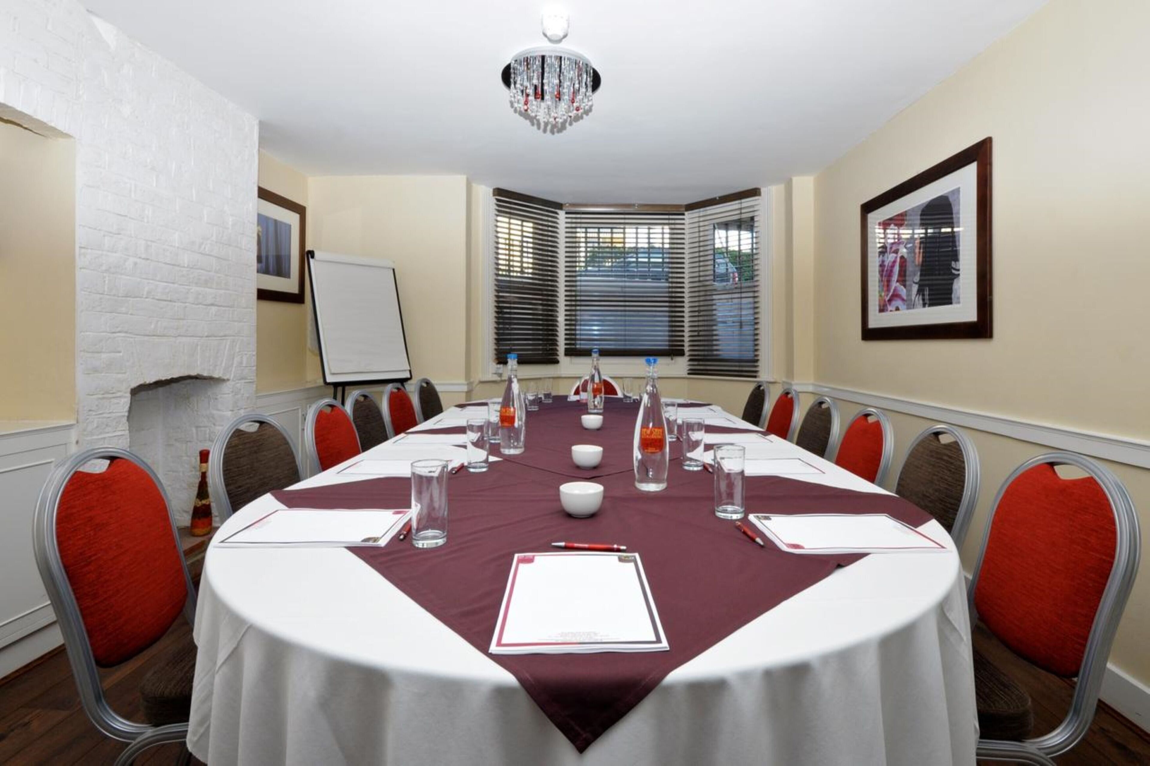 A conference room with a white table, red chairs, a whiteboard, and a window with blinds.
