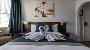 Habitación de hotel con cama, dos mesitas de noche, lámpara, silla, un cuadro en la pared y vistas al exterior a través de la ventana.