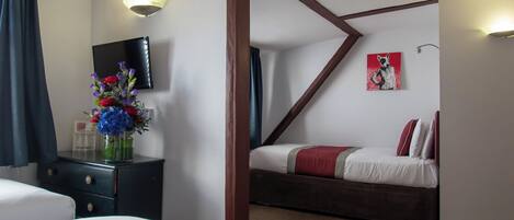 Une chambre d’hôtel avec deux lits, une télévision, un bureau agrémenté d’un vase de fleurs et un tableau au mur.