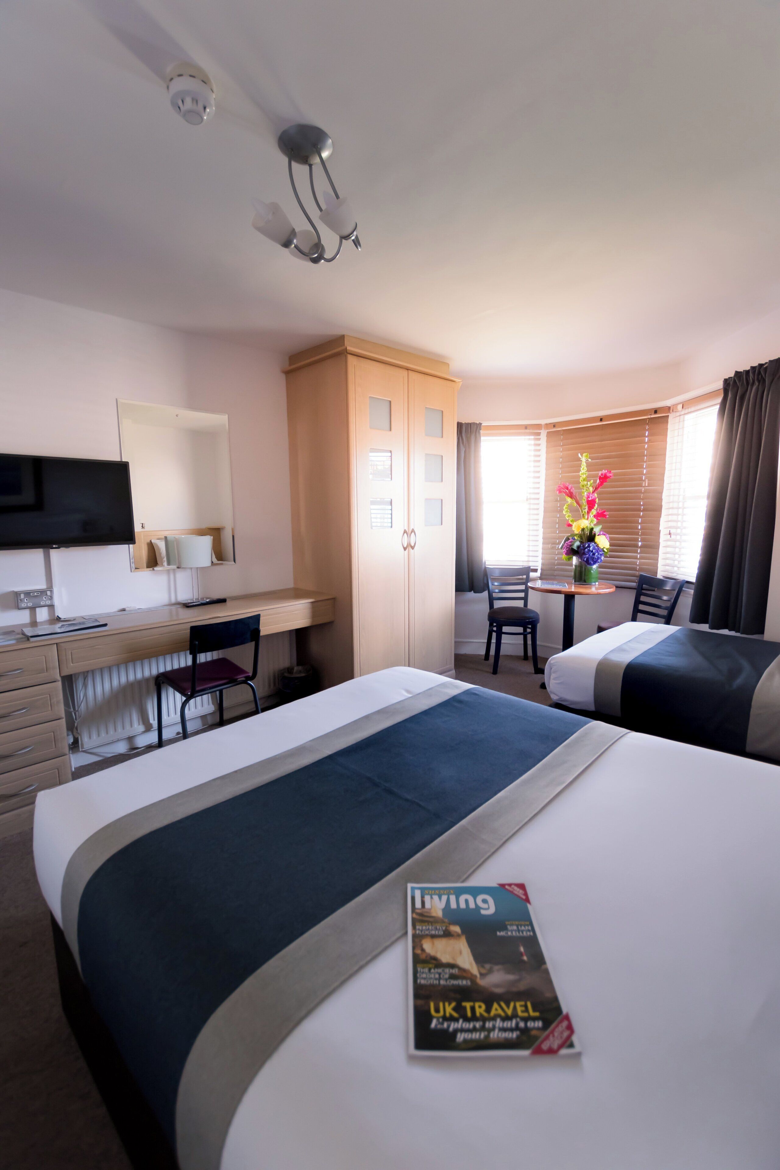 A hotel room with two beds, a desk, a TV, and a window with curtains.