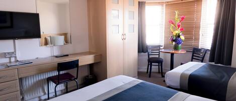 A hotel room with two beds, a desk, a TV, and a window with curtains.