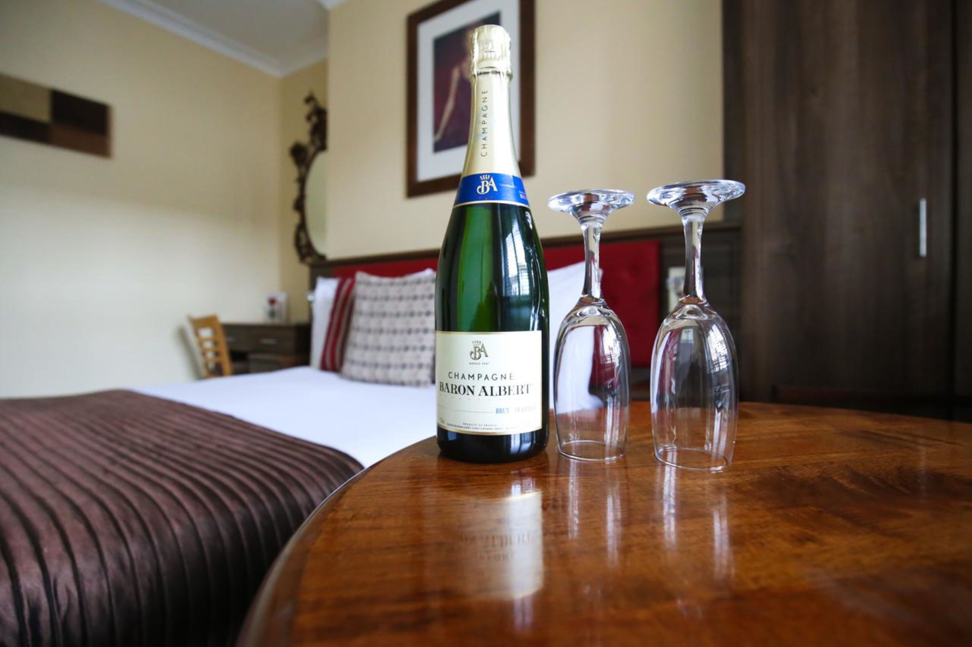 Una botella de champán y dos copas de vino sobre una mesa de madera en una habitación de hotel.
