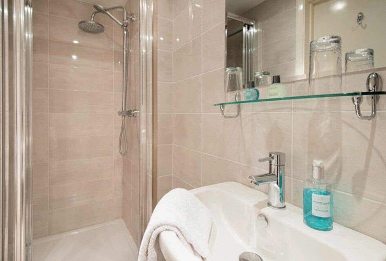 A modern bathroom with a glass shower enclosure, a white sink with a glass shelf above it, and a mirror.