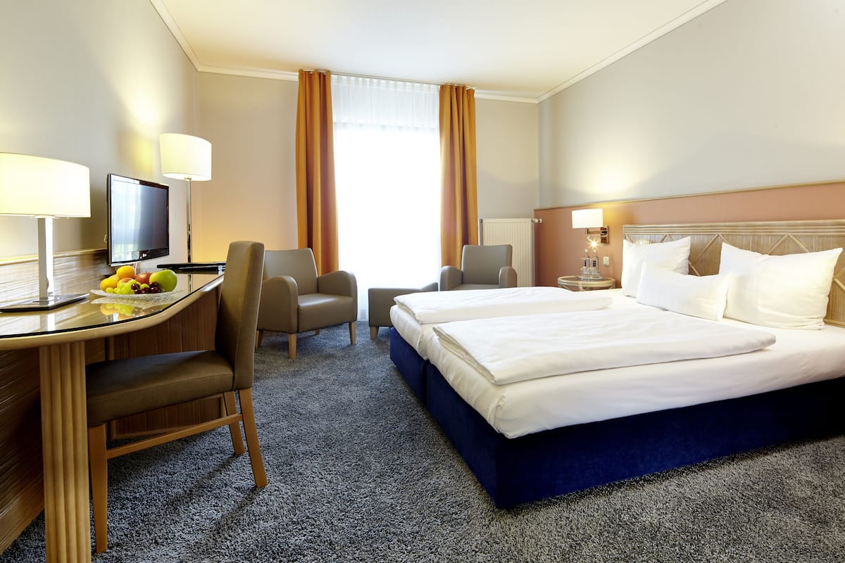 A hotel room with a desk, two chairs, a bed, and a TV.
