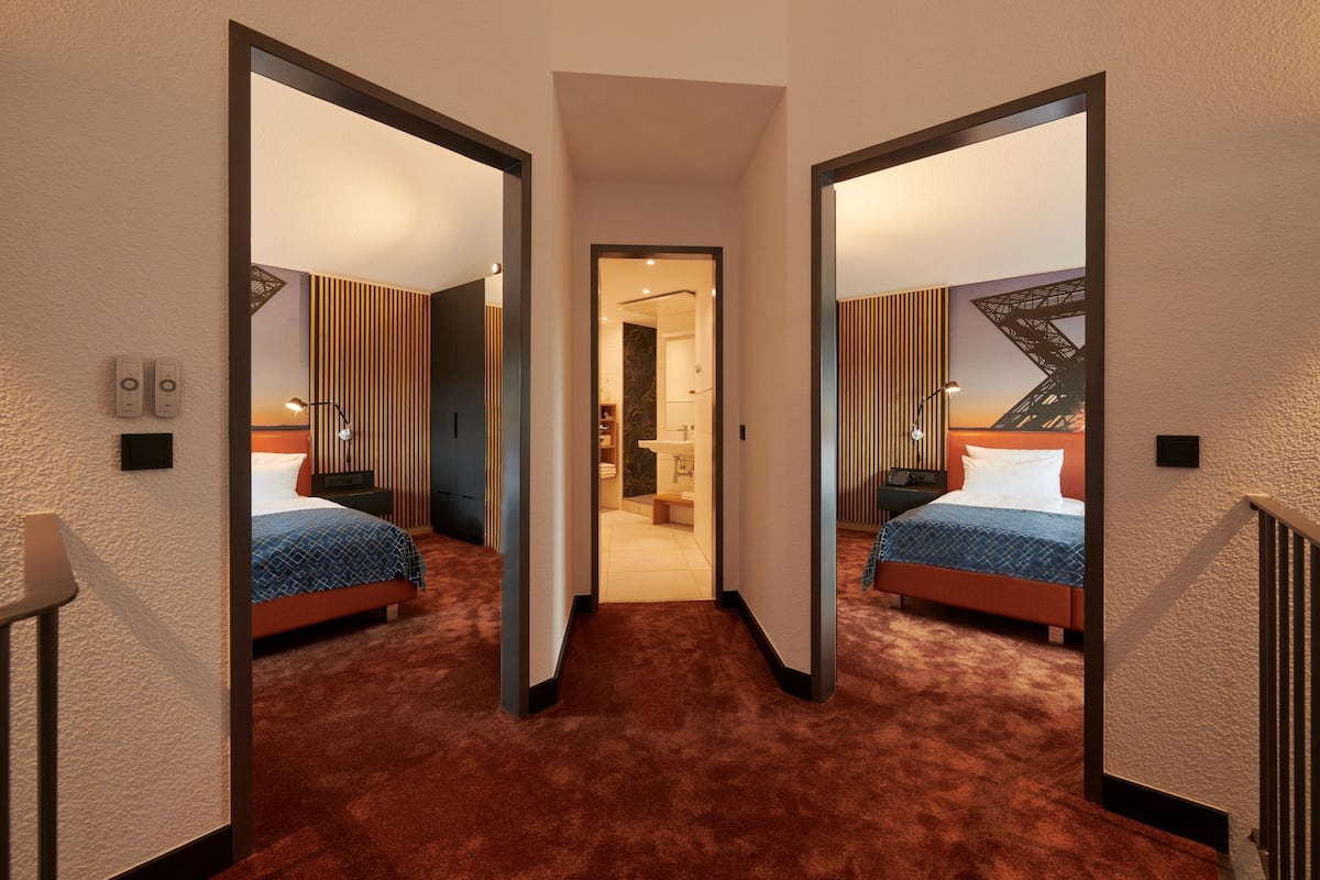 A hotel room with two beds, a carpeted floor, a wooden panel wall, and a view of the cityscape.