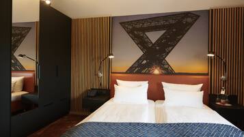 A hotel room with a large bed, a nightstand with a lamp, a seating area with a couch, and a wall with a geometric design.