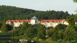 Un hotel con una torre central, rodeado de abundante vegetación y un lago.
