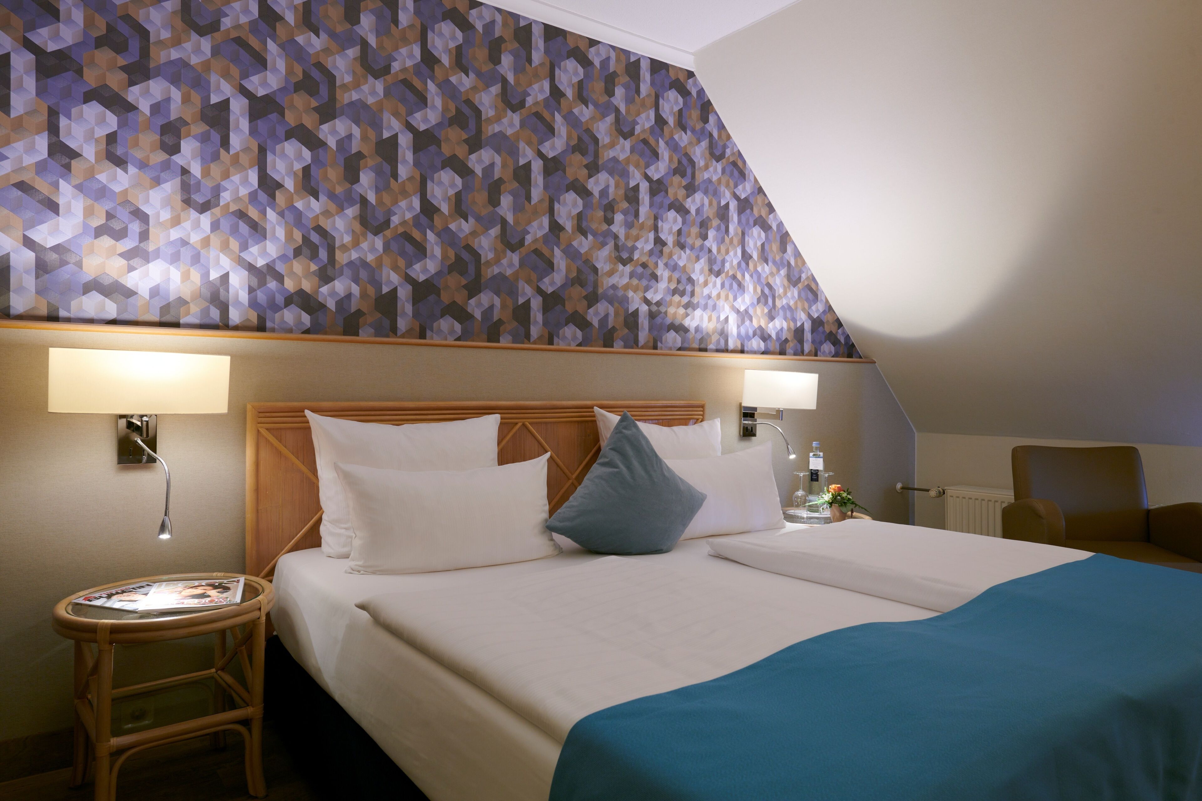 A hotel room with a bed, two bedside tables, a lamp, and a patterned ceiling.