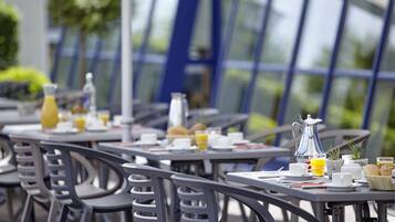 A dining area with tables set for breakfast, including plates, cups, and a pitcher of juice.