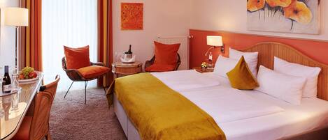 Una habitación de hotel con cama, una silla, una mesa con frutero y un cuadro en la pared.
