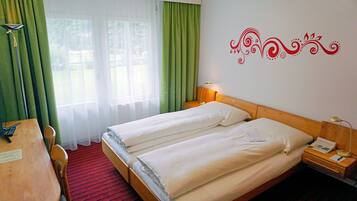 A hotel room with two beds, a desk, a chair, a telephone, and a lamp.