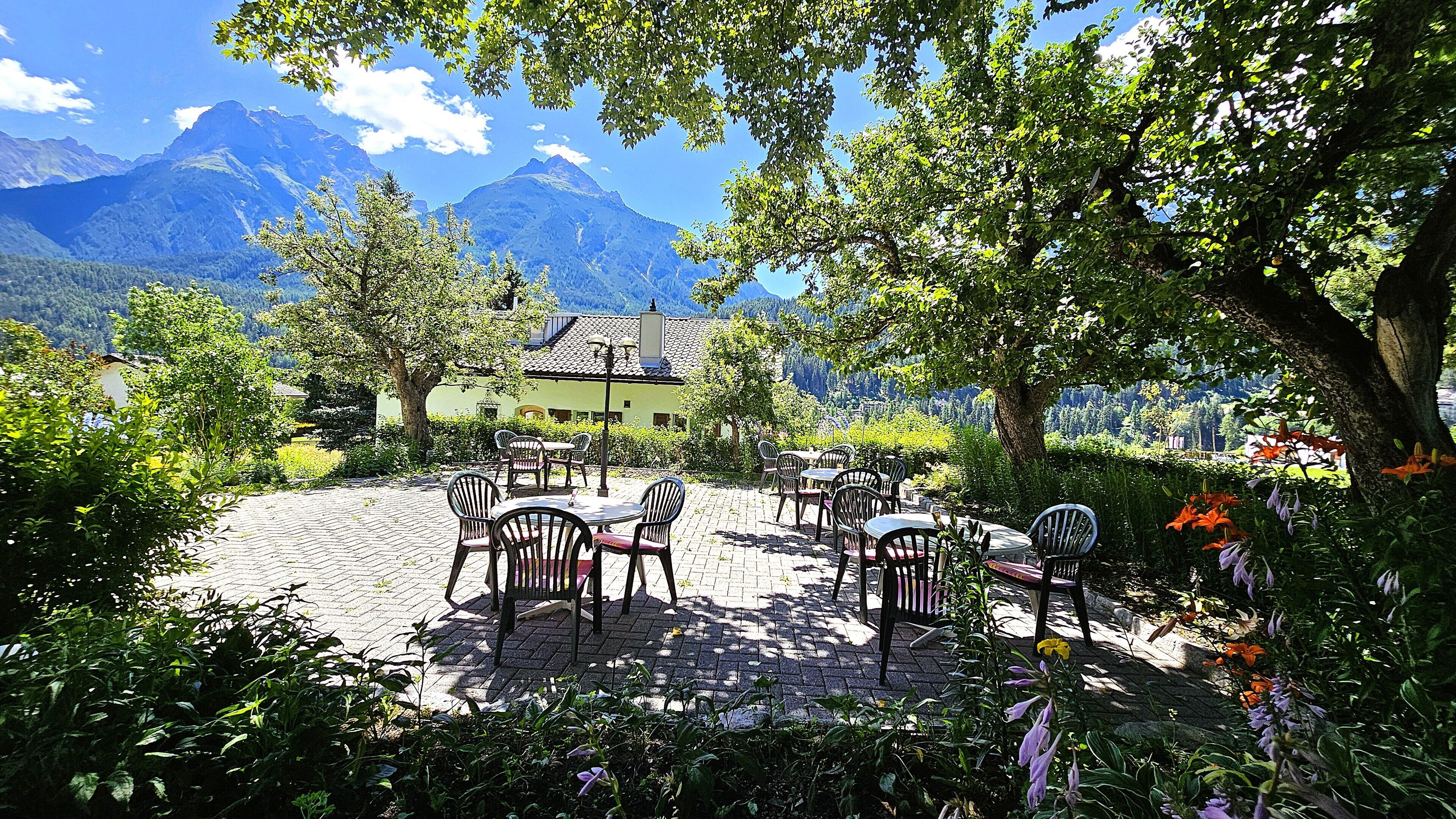 A patio with outdoor seating, a building with a sloped roof, and mountains in the background.