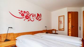 Une chambre d’hôtel avec deux lits, une tête de lit en bois, un motif floral rouge sur le mur, un miroir et une porte en bois.