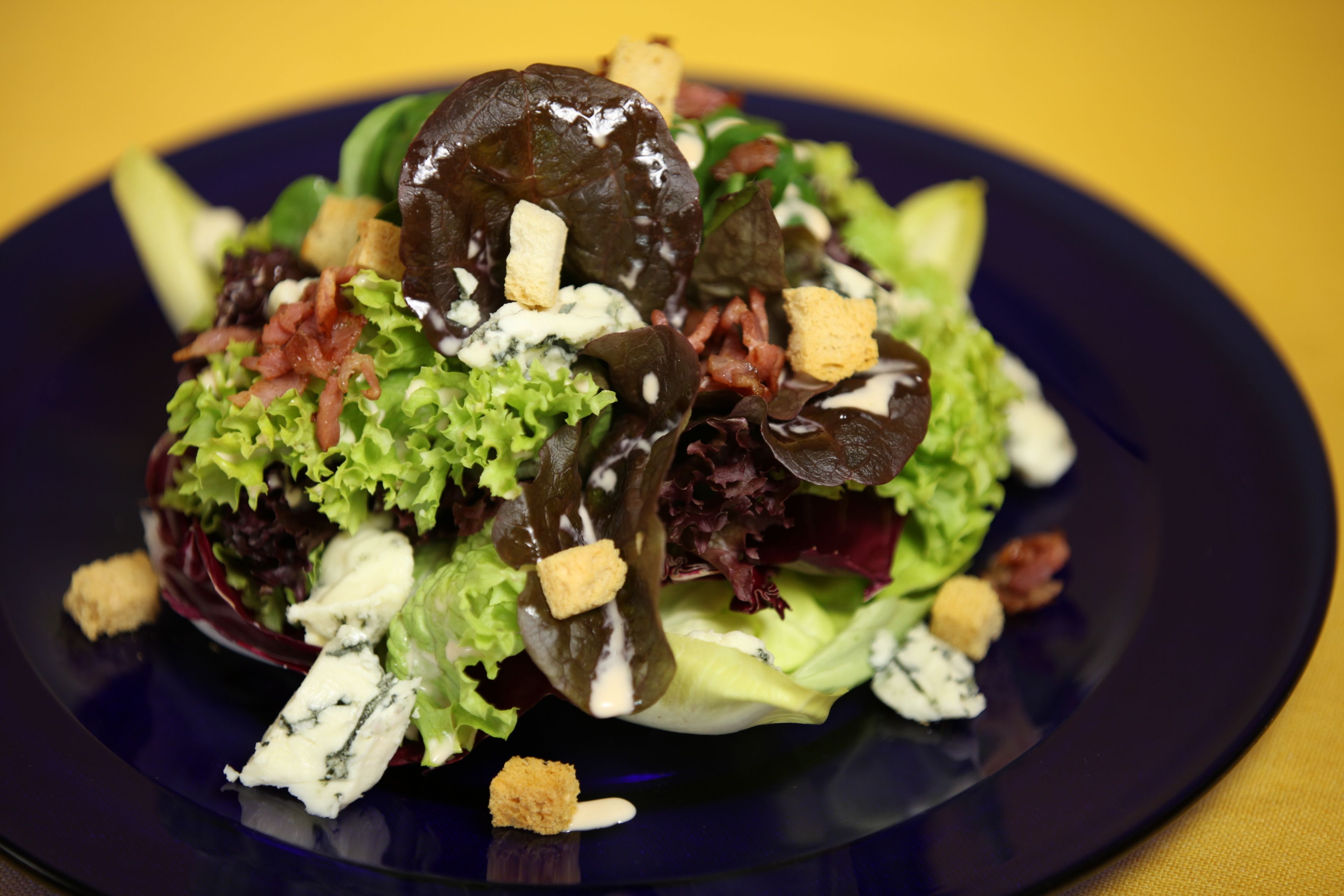 Salada com diversas folhas verdes, croutons e um molho cremoso em um prato.
