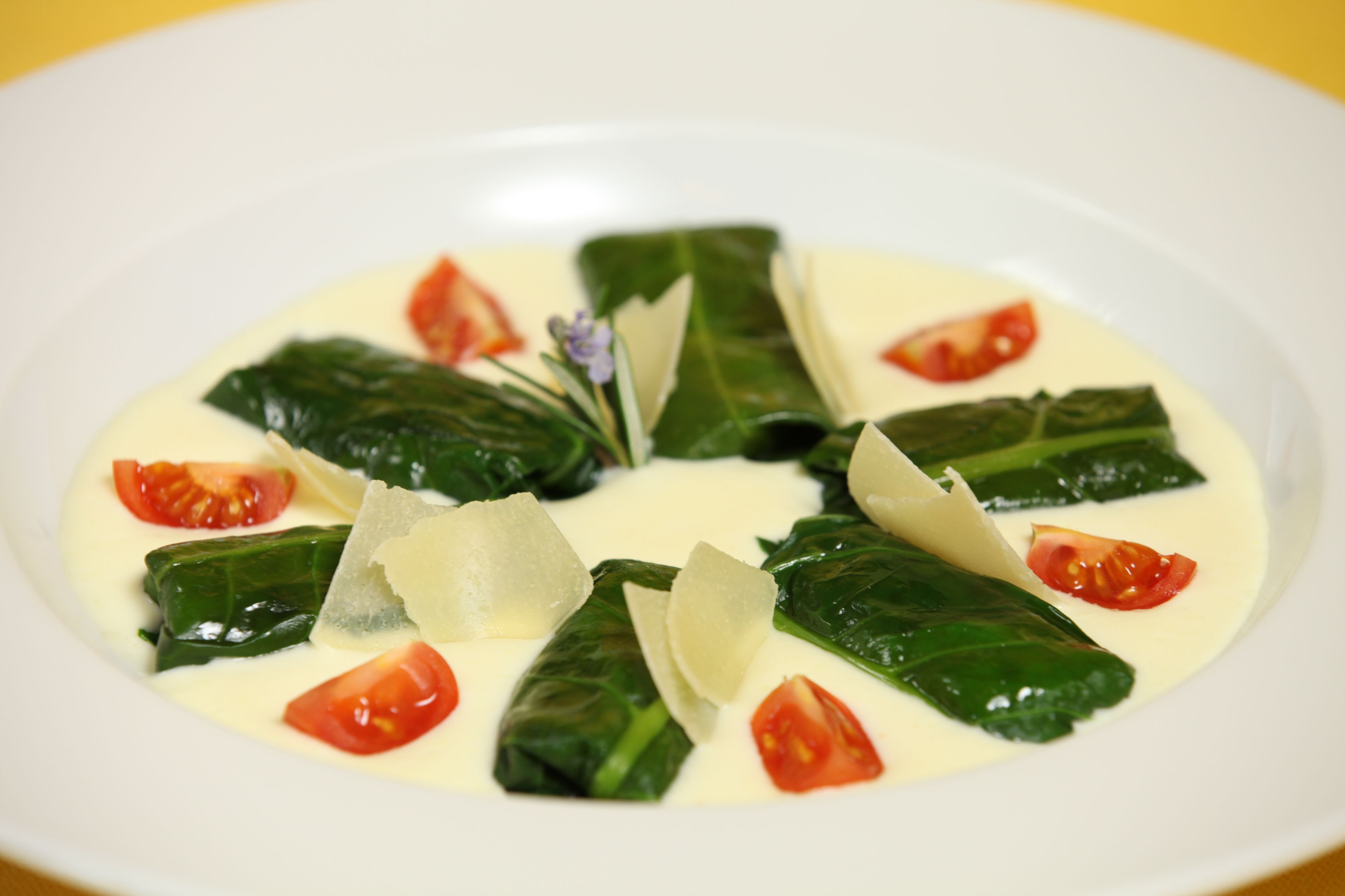 Un plato de hojas de parra rellenas con salsa cremosa, adornado con tomates cherry y queso.