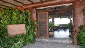 A hotel entrance with a stone sign reading "AURA DEL MAR", a wooden door, and a tiled floor. - Hotel Aura del Mar (Zihuatanejo)