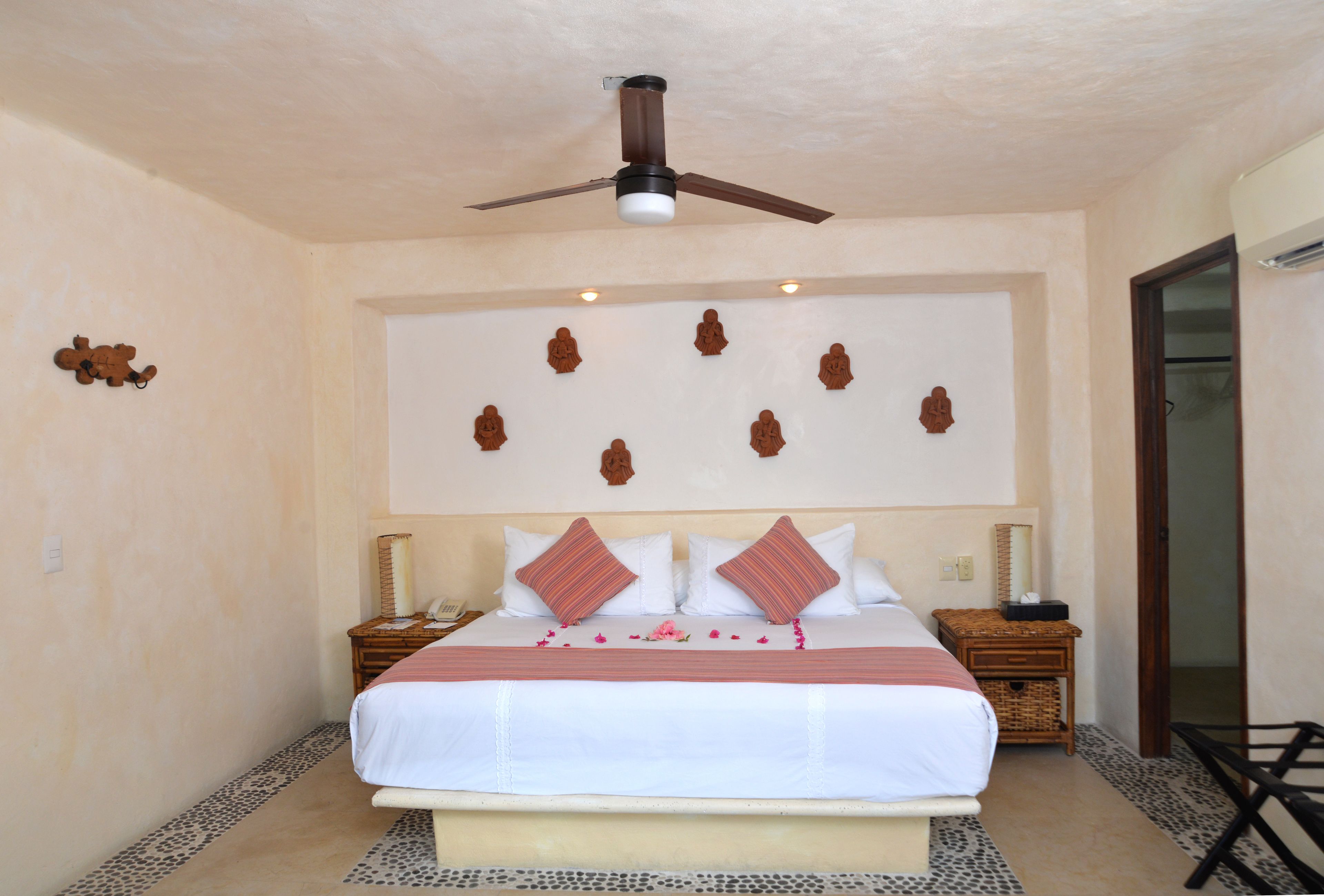 A neatly arranged bedroom with a bed, a ceiling fan, a wall-mounted clock, and a small table with a lamp.