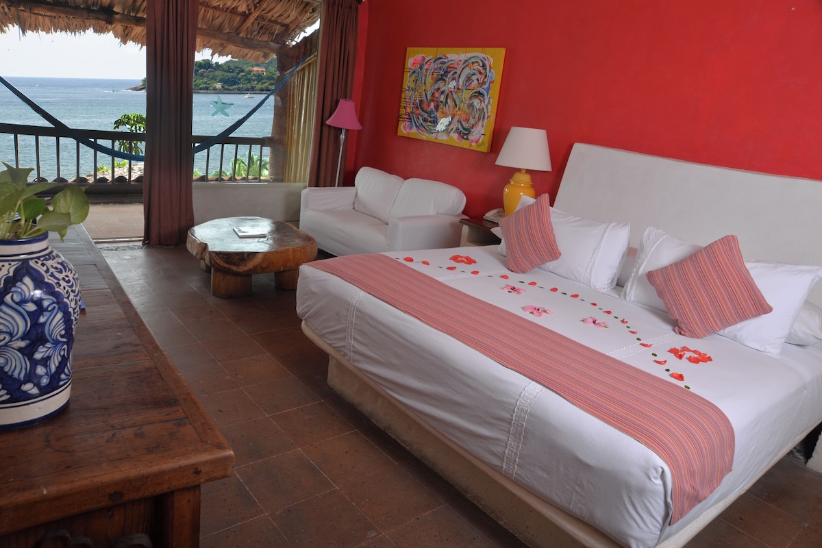 Een hotelkamer met een bed, een bank, een tafeltje en uitzicht op zee.