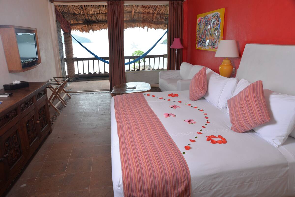 Une chambre d’hôtel avec un lit, une télévision, un bureau et un balcon donnant sur la mer.