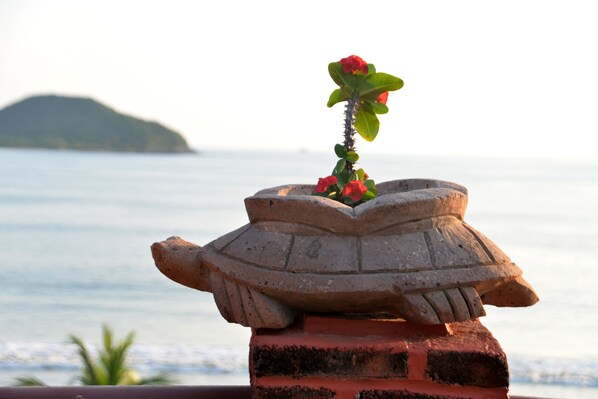 A stone planter with a cactus and red flowers, set against a backdrop of a calm sea and a distant island.
