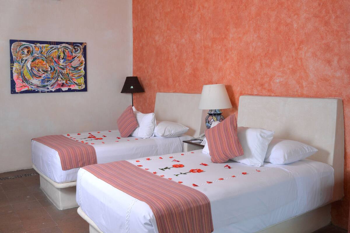 Une chambre d’hôtel avec deux lits, un ventilateur de plafond, un tableau et un sol carrelé.
