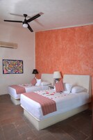 Una habitación de hotel con dos camas, un ventilador de techo, un cuadro y suelo de baldosas.