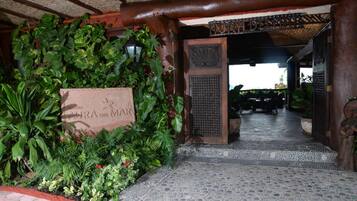 Entrada de um resort tropical, com uma placa indicando 'LAURA DEL MAR' e uma área de varanda coberta.