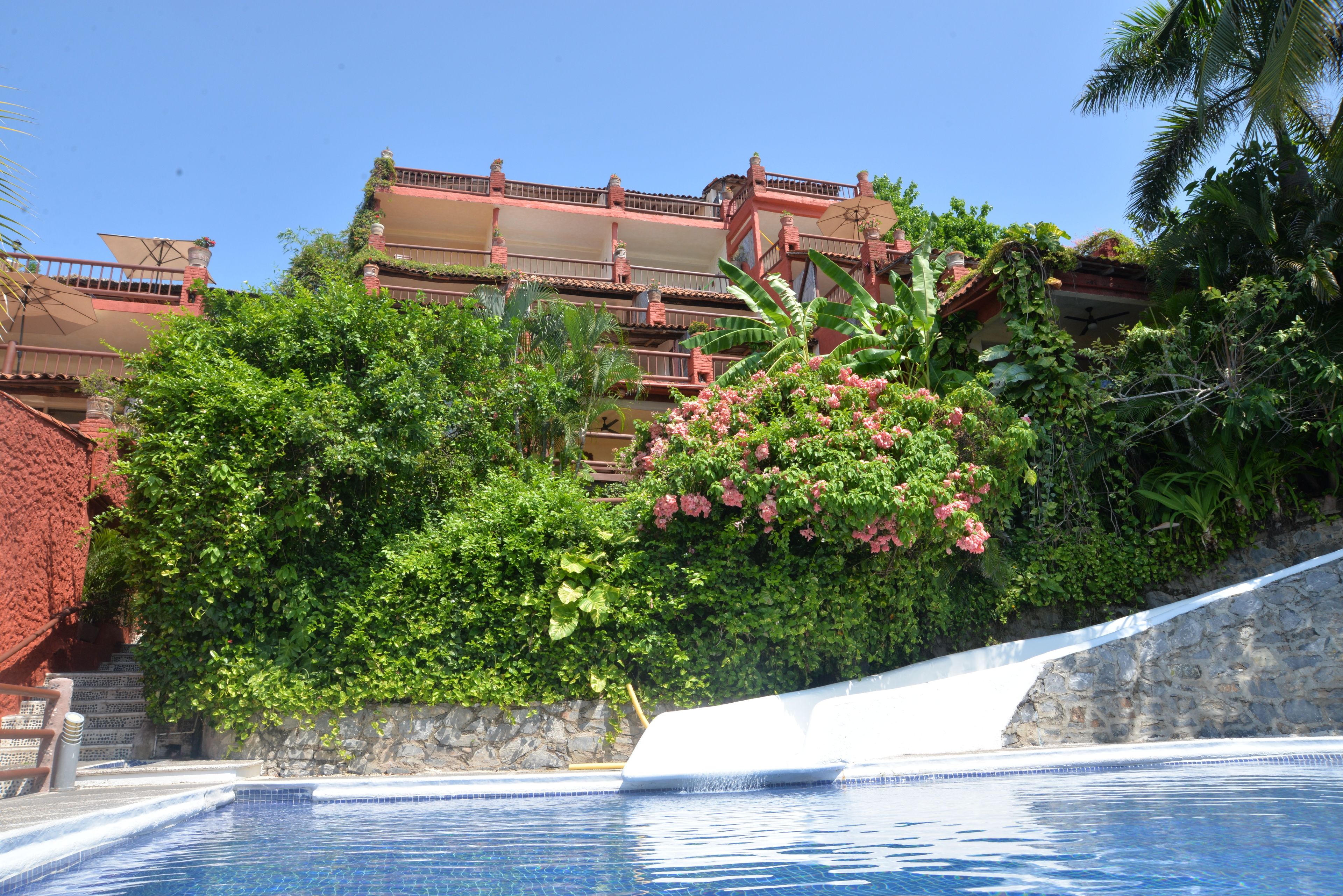 Une piscine bordée d’un mur de pierre et, au fond, un bâtiment rouge doté de balcons.