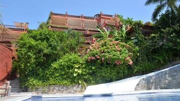 Une piscine bordée d’un mur de pierre et, au fond, un bâtiment rouge doté de balcons.