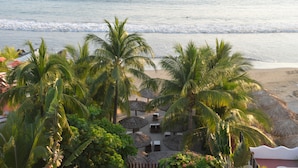 A beachside resort with palm trees, thatched umbrellas, and lounge chairs. - Hotel Aura del Mar (Zihuatanejo)