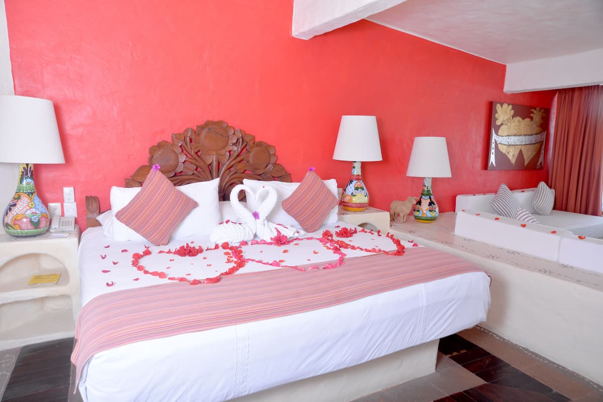 Une chambre d’hôtel avec un grand lit, une literie blanche et rouge, et un mur d’accent rouge.