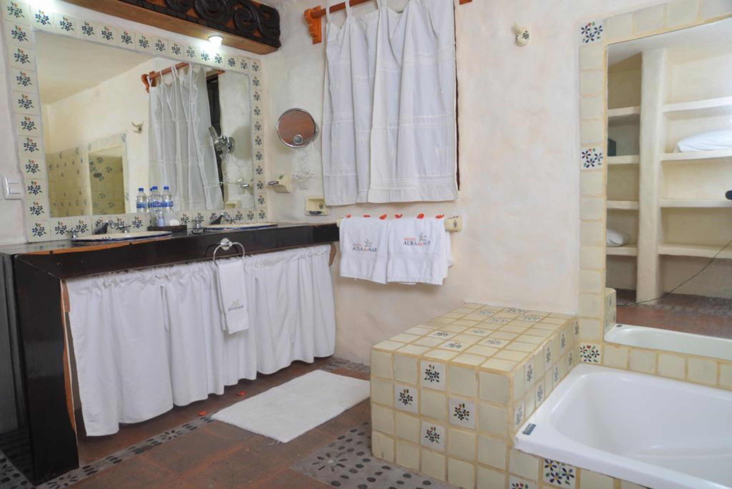 A bathroom with a tiled floor, a bathtub, a sink with a mirror, and a towel rack.