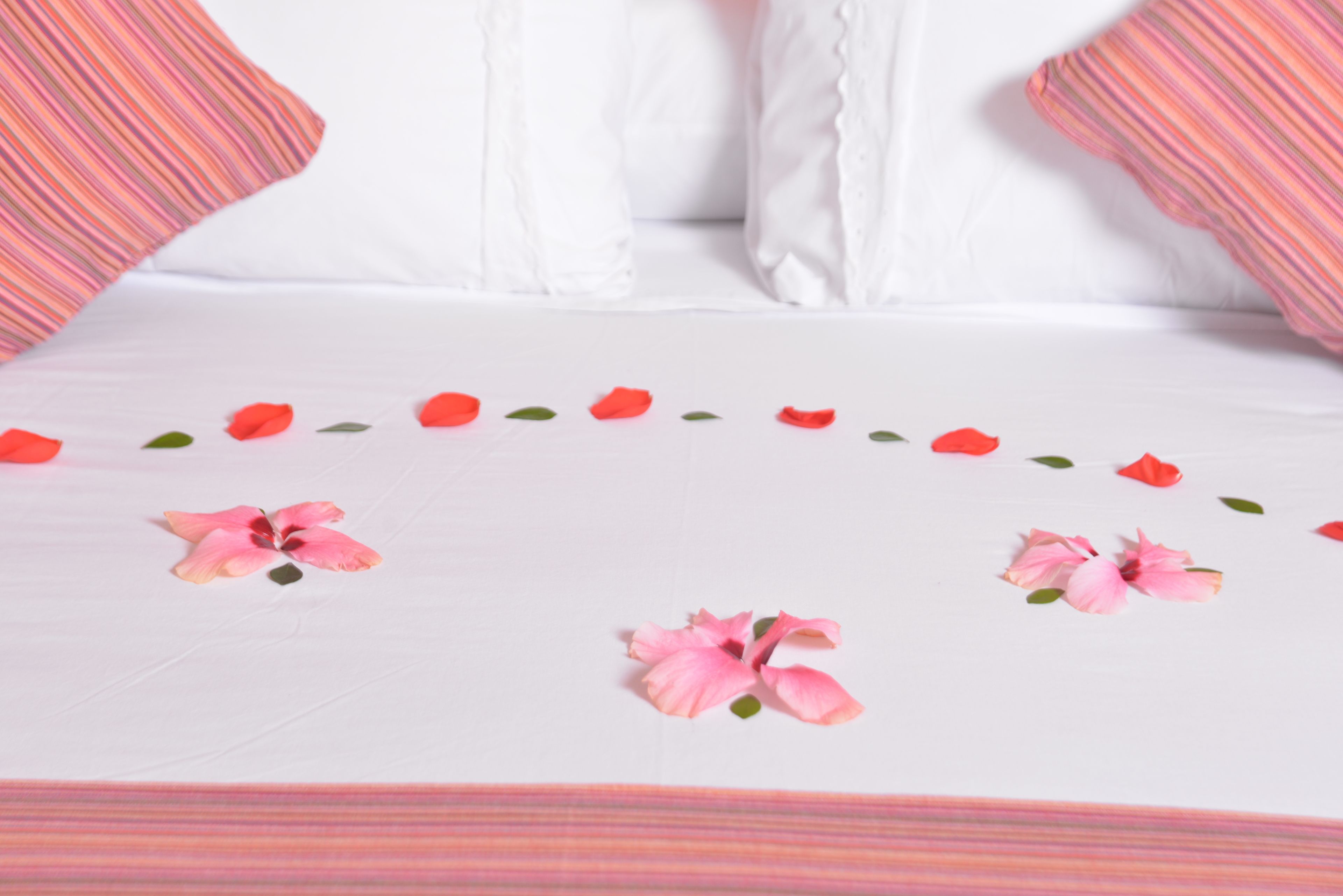 Una cama con ropa de cama blanca, adornos florales rosas y almohadas a rayas.