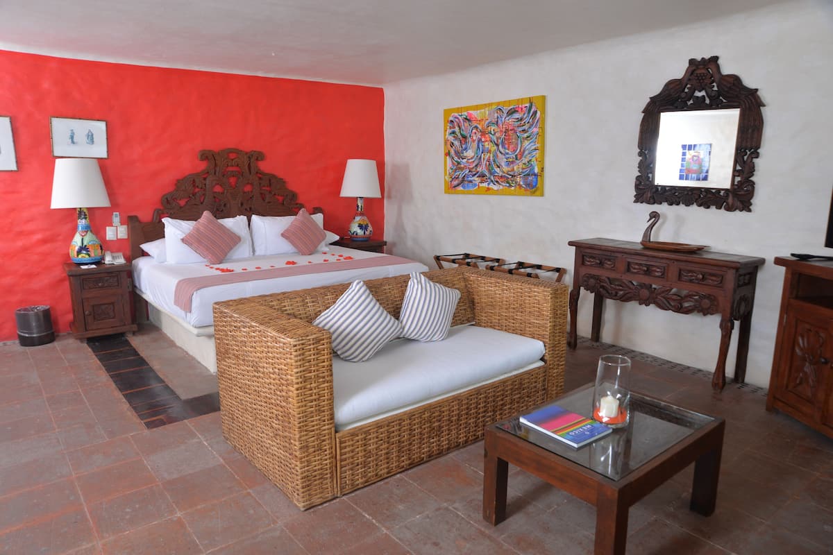 Une chambre d’hôtel avec un lit, un canapé en osier, une commode en bois et une table basse en verre.