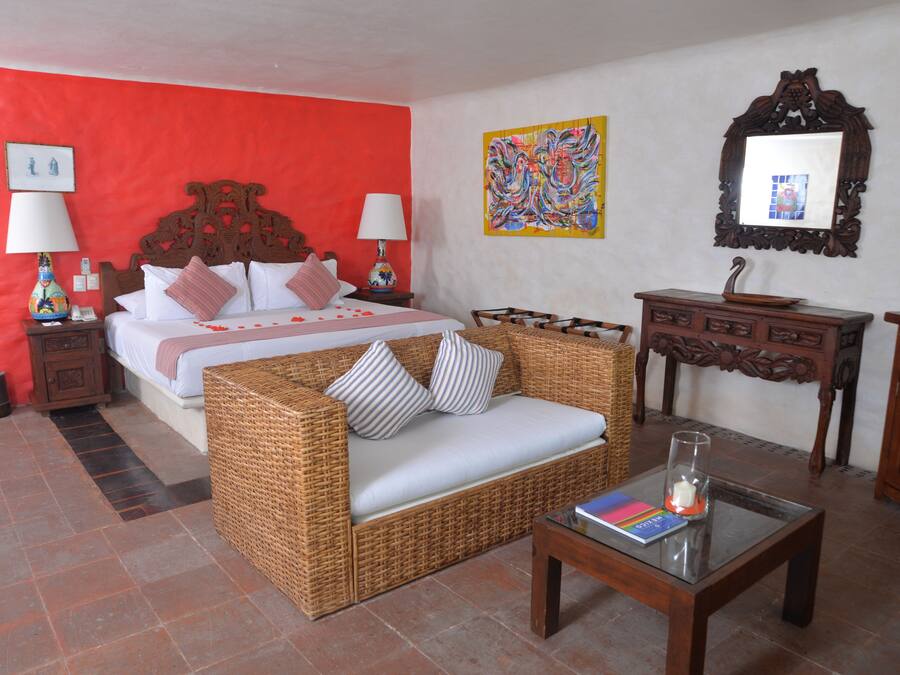Una habitación de hotel con una cama, un sofá de mimbre, un aparador de madera y una mesa de centro de vidrio.