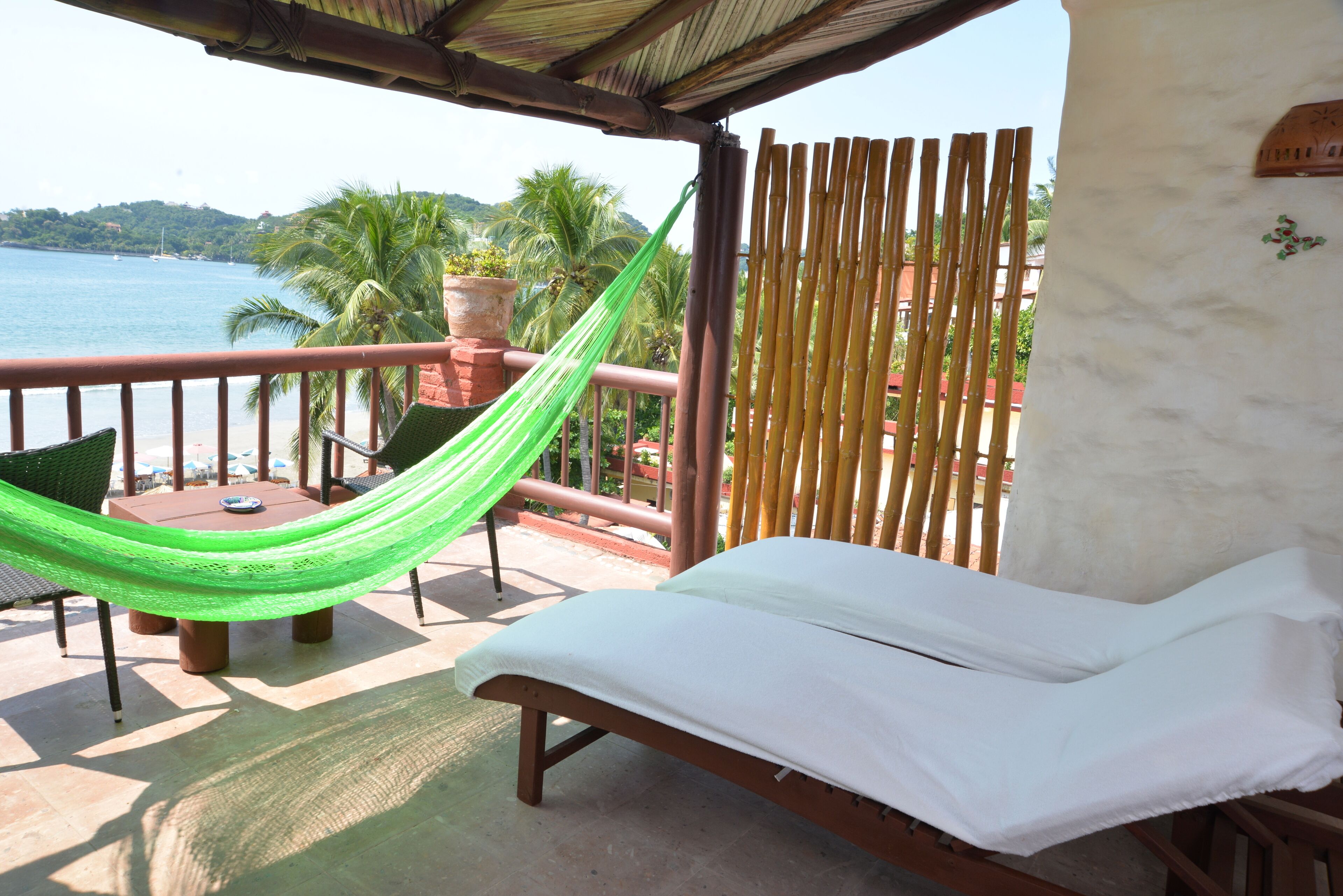 A hammock on a balcony with a view of the sea and palm trees.