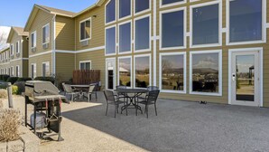 Un immeuble résidentiel doté d’un patio comprenant un barbecue, des sièges d’extérieur et de grandes fenêtres.