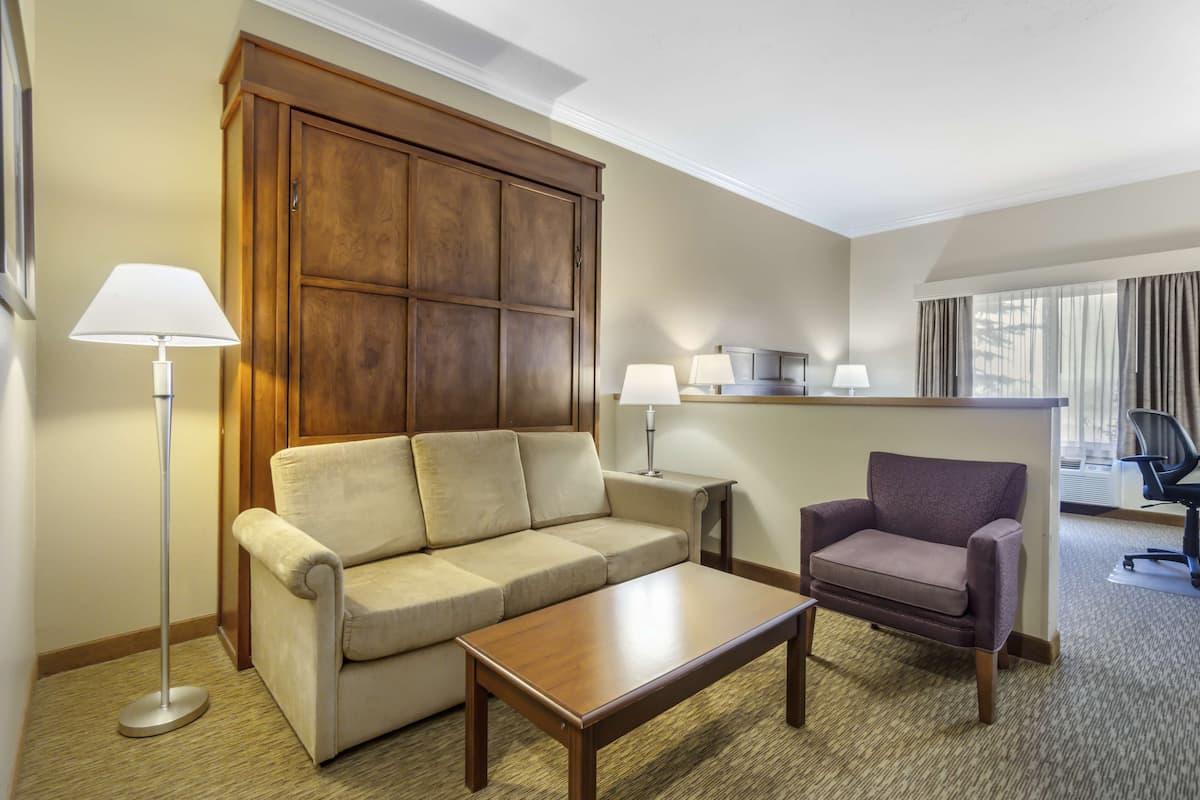 A hotel room with a sofa, armchair, coffee table, and a large wooden cabinet.