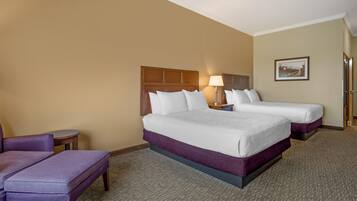 A hotel room with two beds, a small table, a chair, and a lamp.
