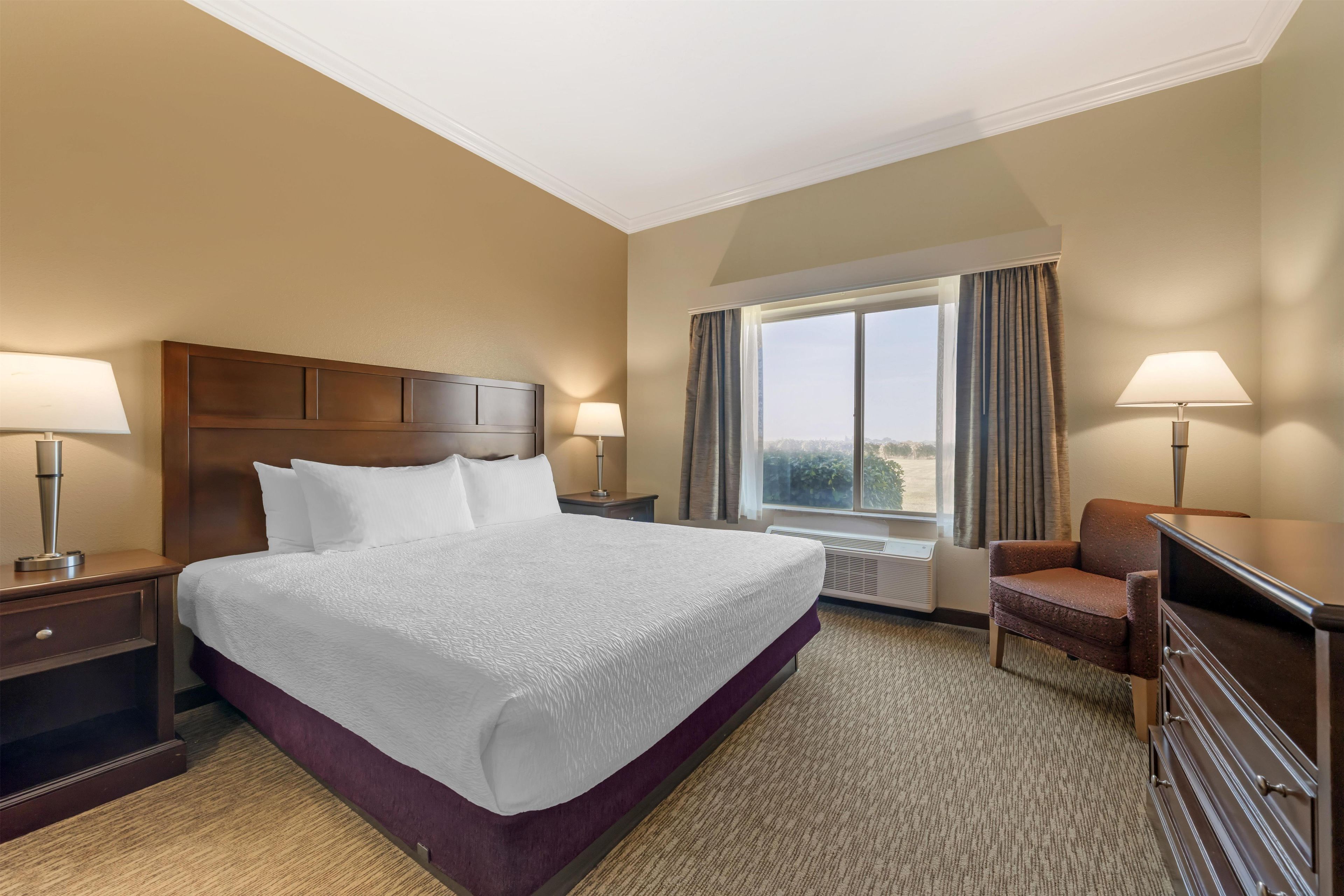 A hotel room with a large bed, two bedside tables with lamps, a chair, a desk, and a window with curtains.
