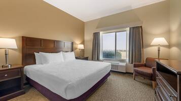 A hotel room with a large bed, two bedside tables with lamps, a chair, a desk, and a window with curtains.