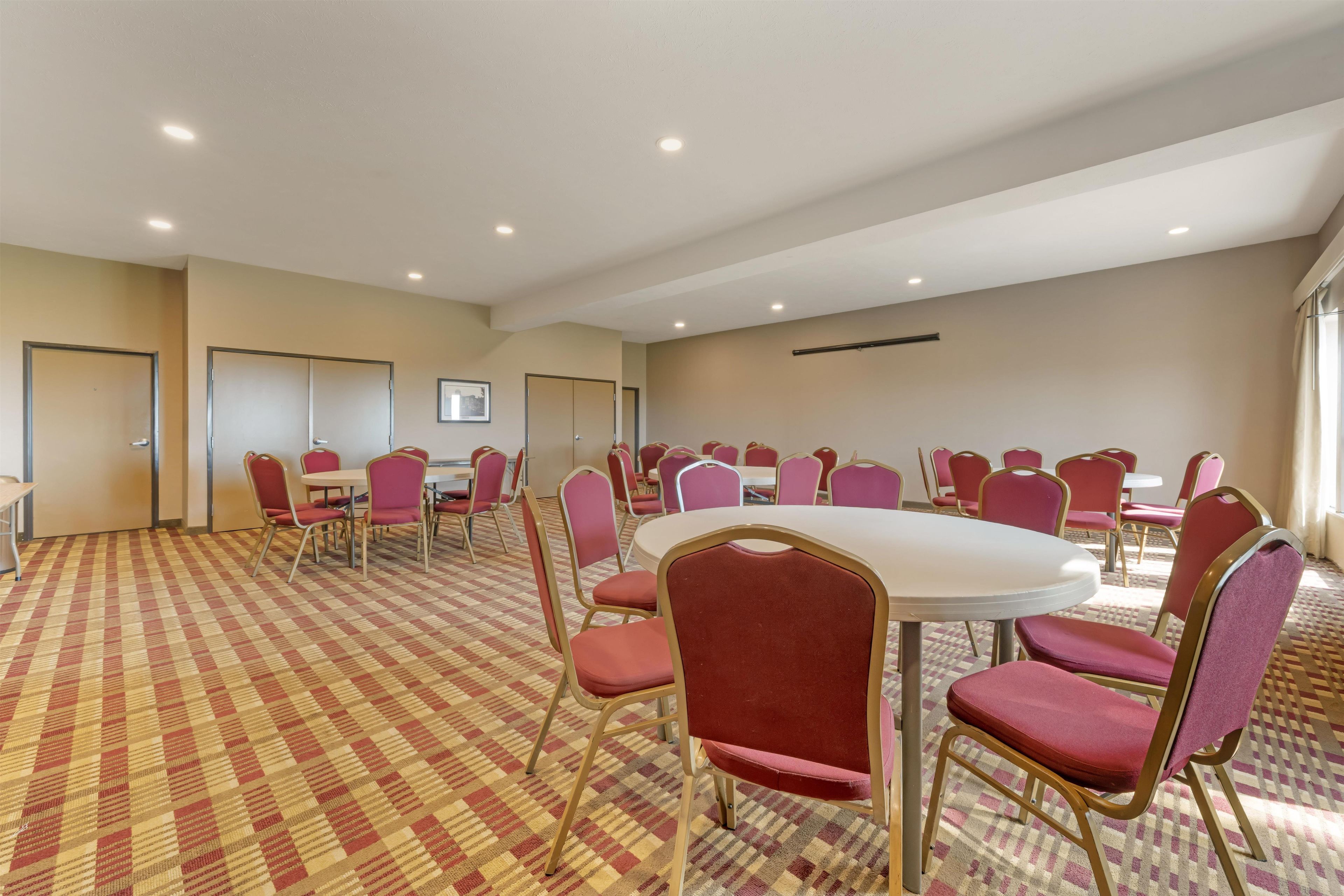 A conference room with a checkered carpet, round tables, and red chairs.