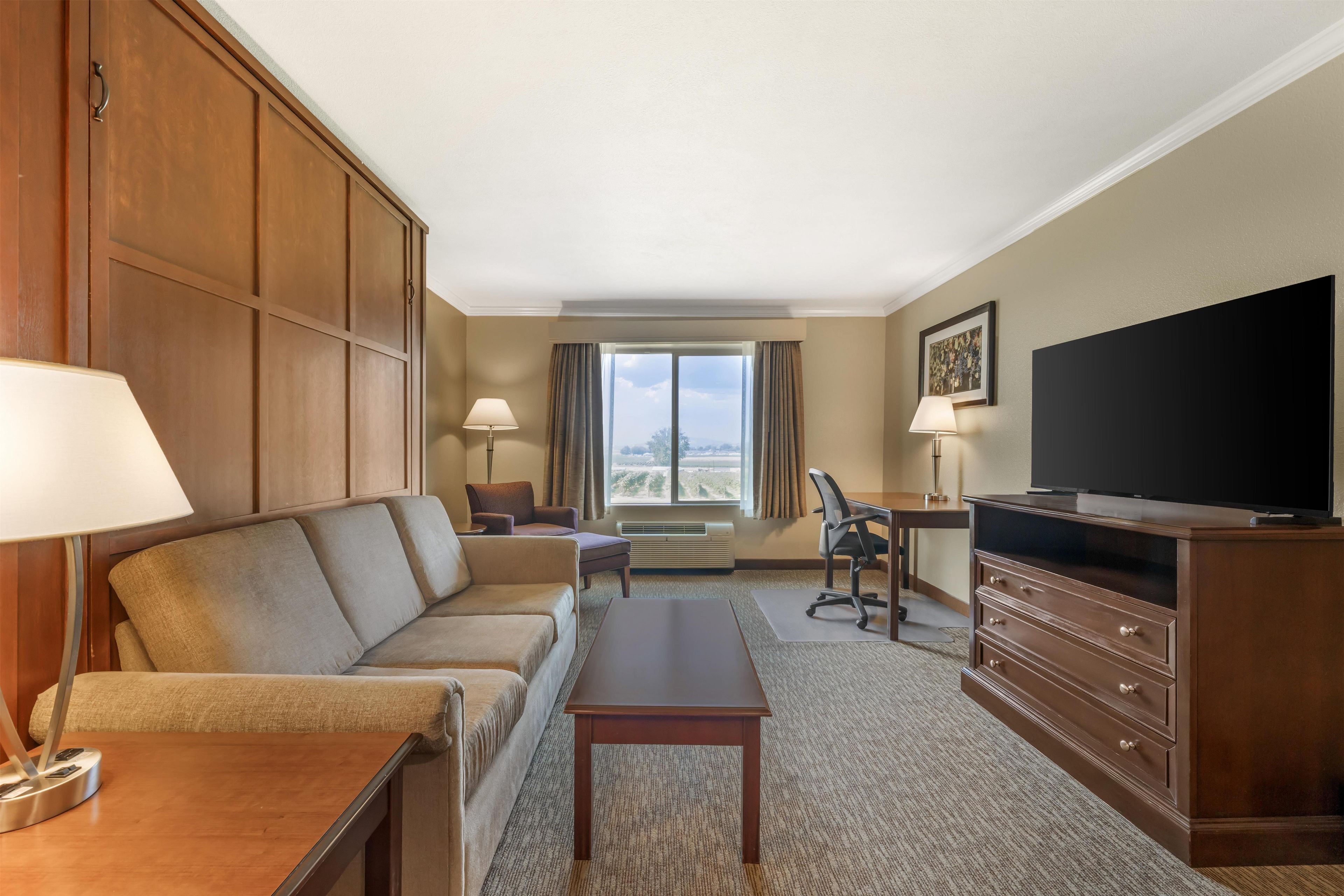 A hotel room with a sofa, a desk, a television, and a window with curtains.
