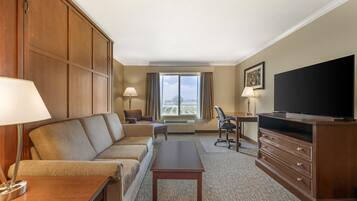 A hotel room with a sofa, a desk, a television, and a window with curtains.