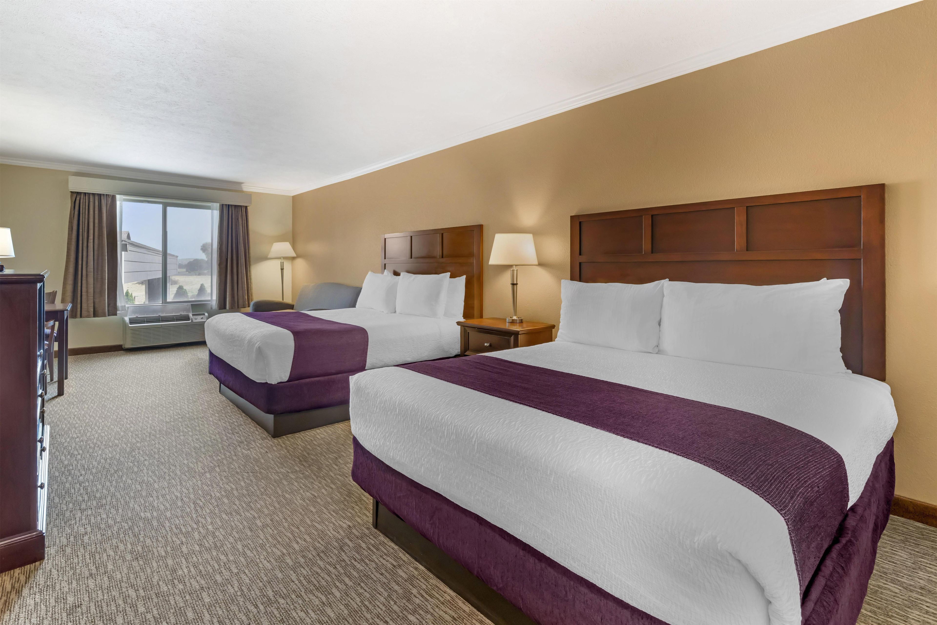 A hotel room with two beds, a desk, a chair, and a window with curtains.